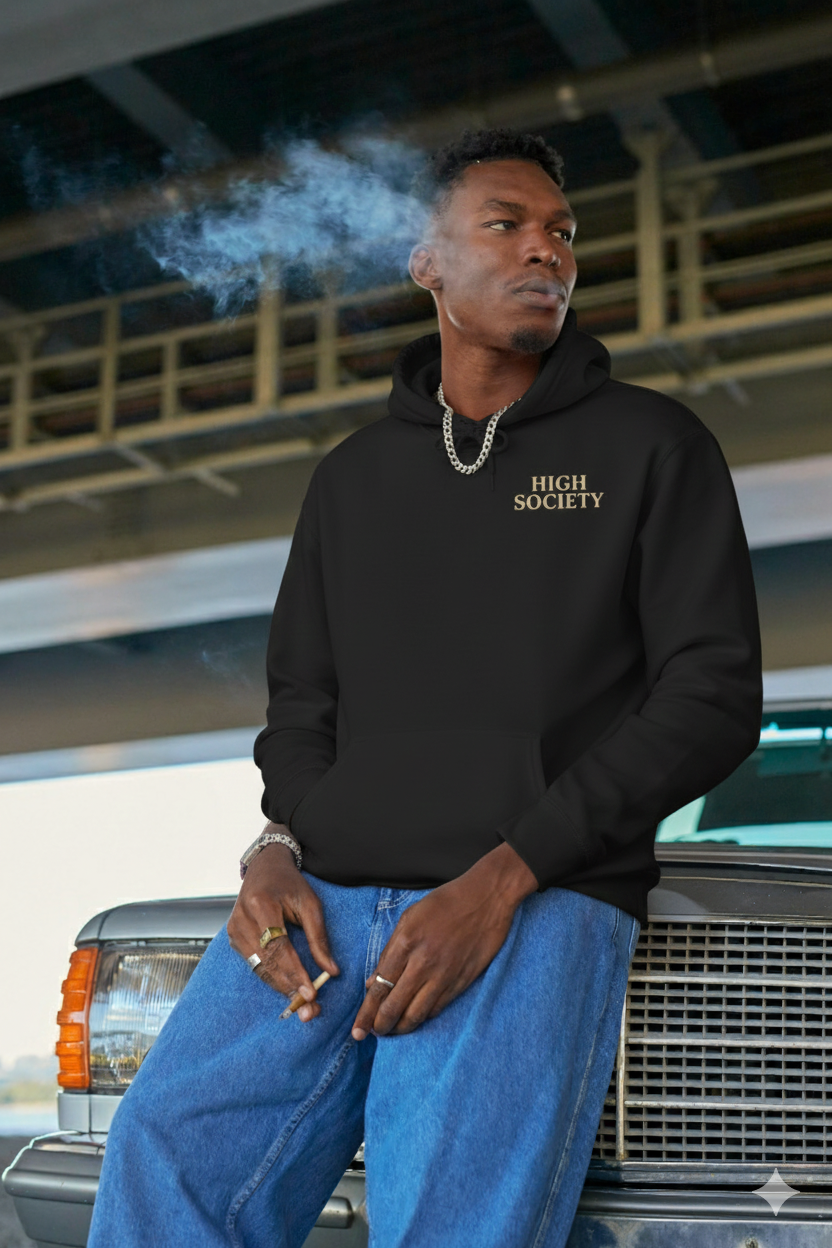 Person wearing a black hoodie with 'High Society' text, leaning against a vehicle under a bridge.