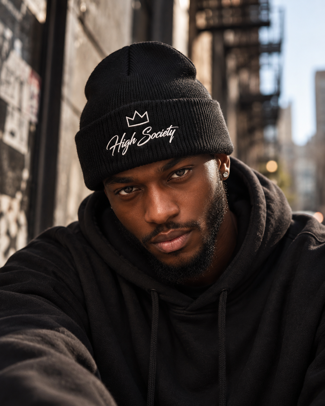 Male model wearing black High Society embroidered beanie in an urban streetwear setting