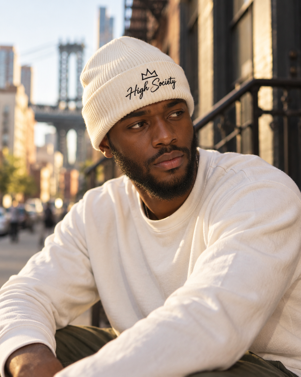 Male model wearing light High Society embroidered beanie in a golden-hour urban setting